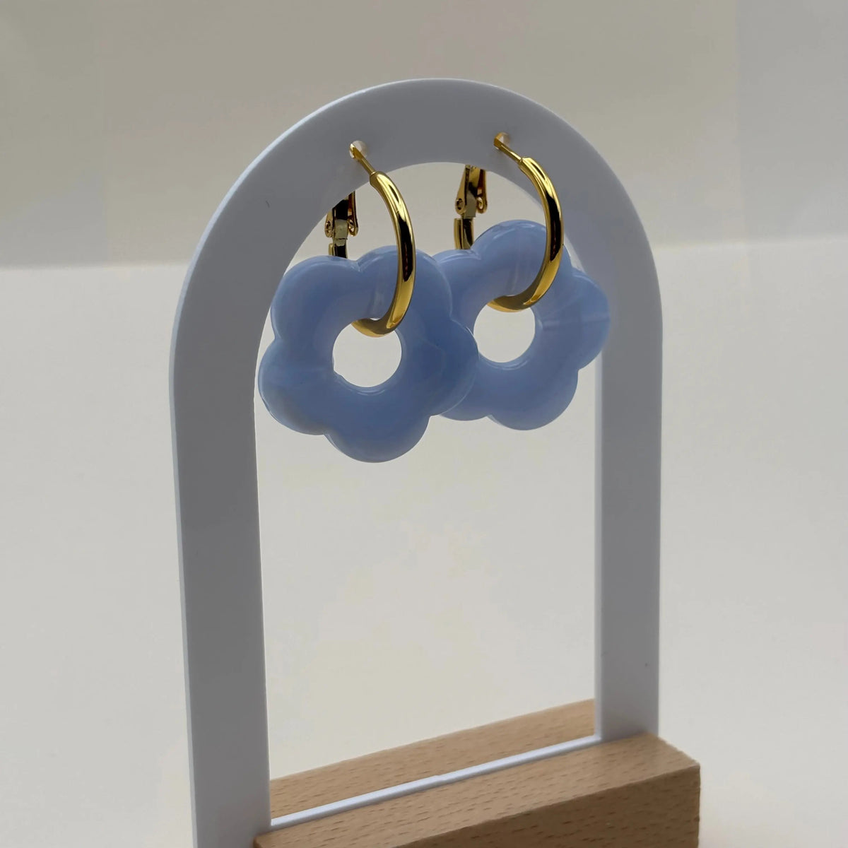 Des boucles d'oreilles dorées façon créoles avec une fleur écrue bleue