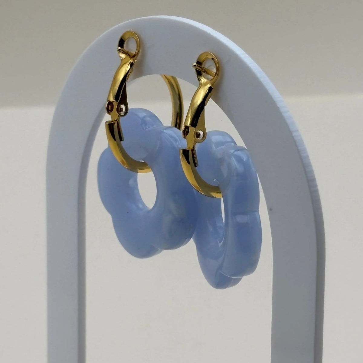 Une paire de boucles d'oreilles dorées façon créoles avec une fleur écrue bleue