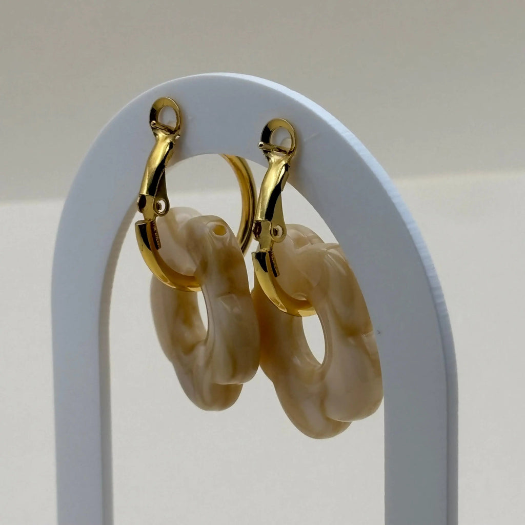 Une paire de boucles d'oreilles dorées façon créoles avec une fleur écrue