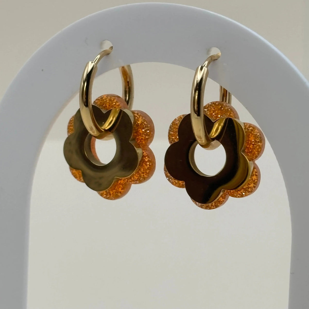 Une paire de boucles d'oreilles dorée façon créole avec une fleur orange et une fleur dorée