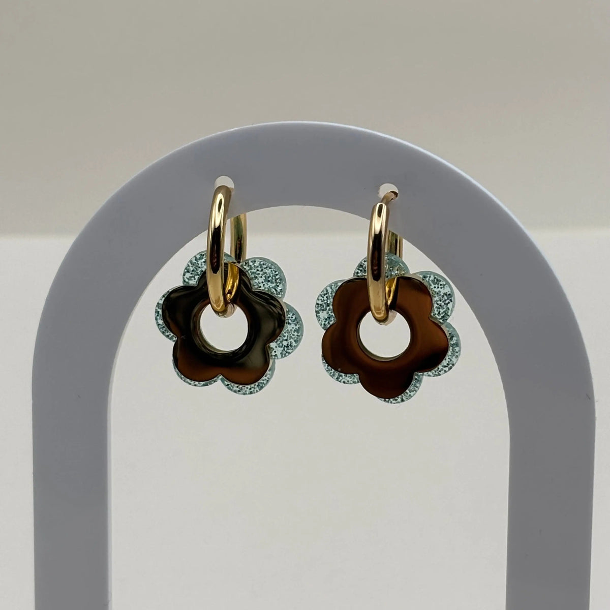 Une paire de boucles d'oreilles dorée façon créole avec une fleur bleue vert et une fleur dorée