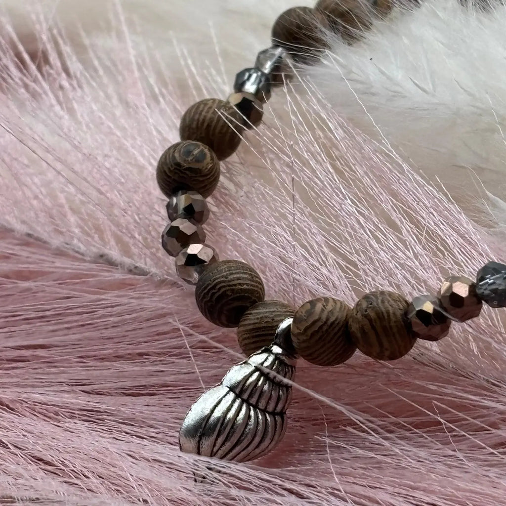 Vue de près d'un bracelet en perles artisanal  avec breloque coquillage argenté et perles en bois sur élastique