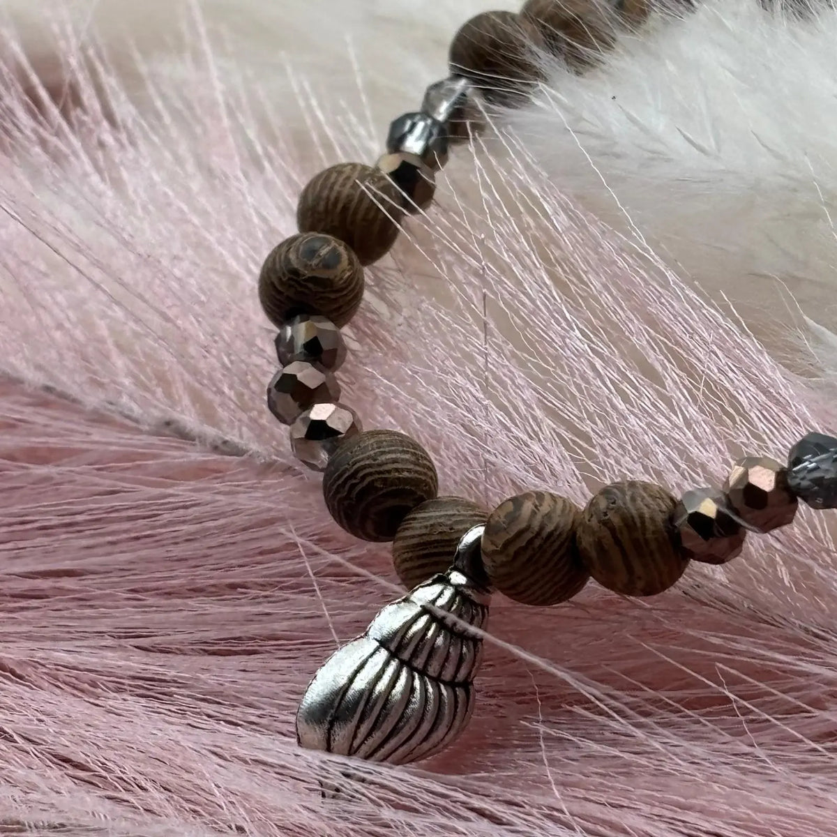 Vue de près d'un bracelet en perles artisanal  avec breloque coquillage argenté et perles en bois sur élastique