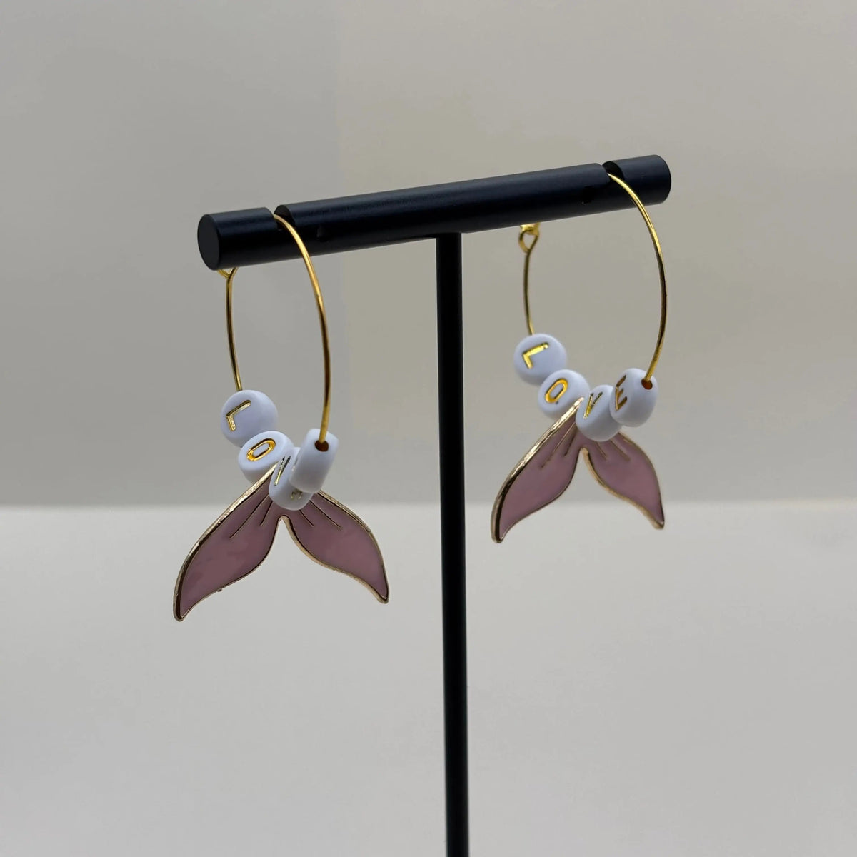 Des boucles d'oreilles créoles dorées avec queue de baleine rose et mot love 