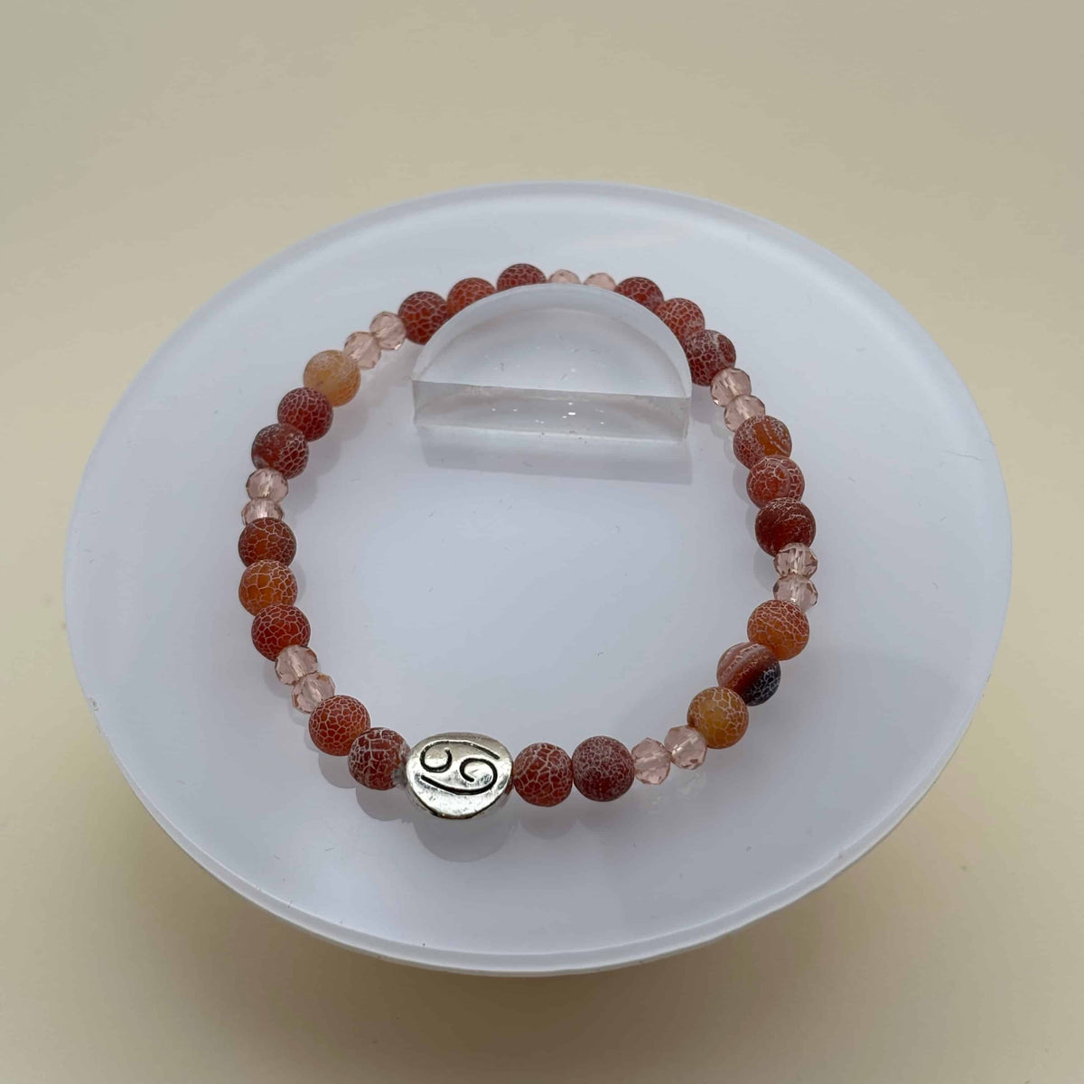 Un bracelet en perles sur élastique avec perles en porcelaine et en verre et médaillon avec le signe zodiaque du cancer