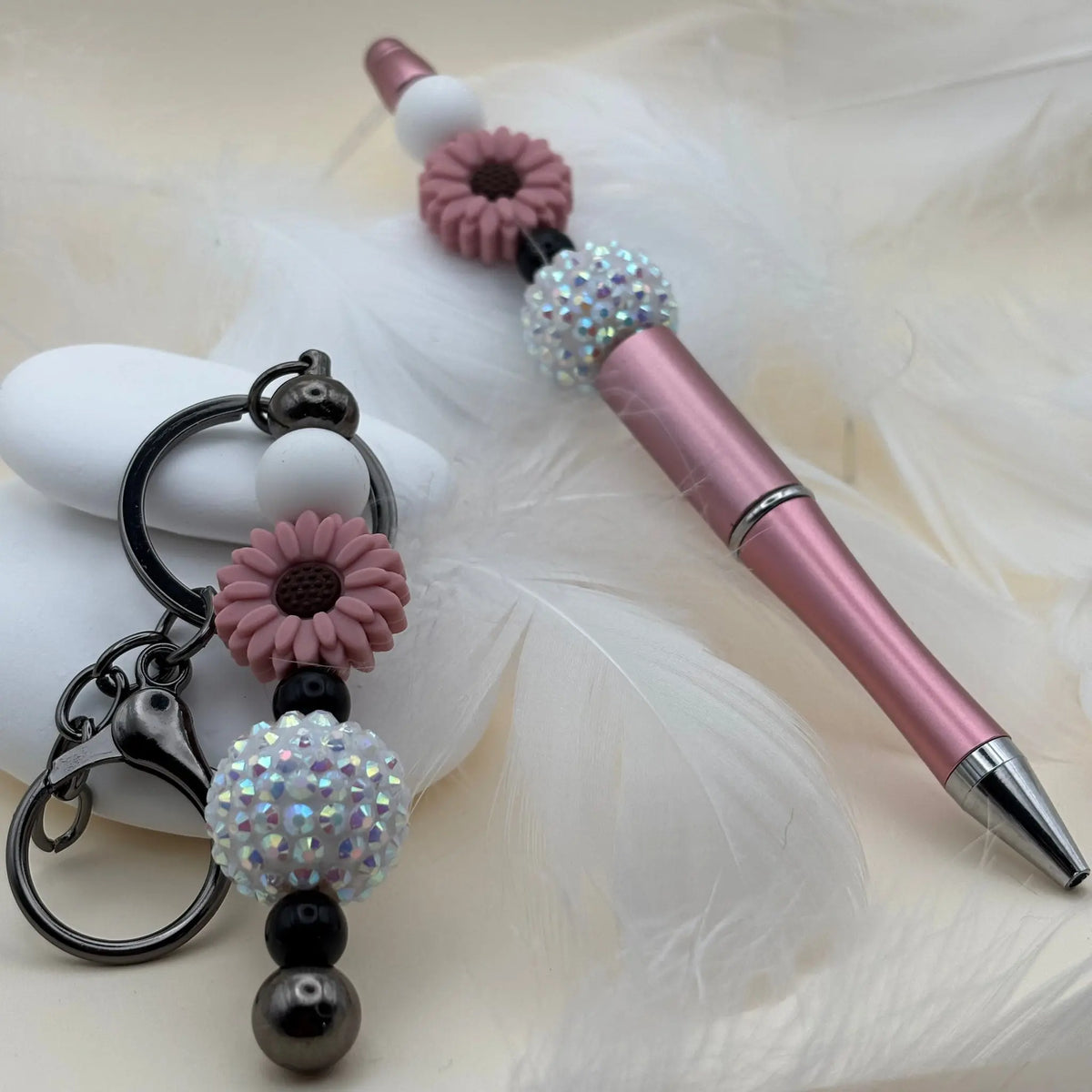 Stylo rose brillant orné de perles blanches, noires et fleurs mauves, accompagné d’un porte-clés assorti décoré de perles irisées.