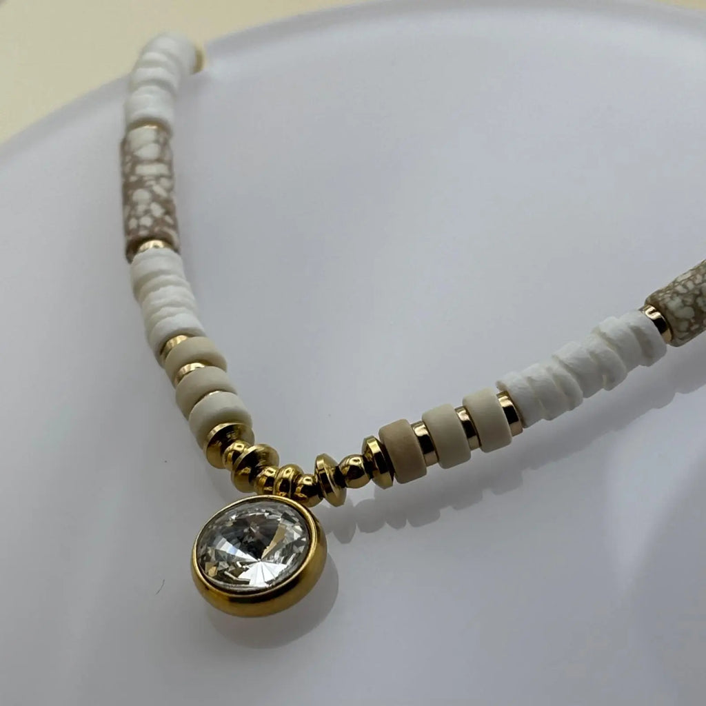 Bracelet doré avec perles plates blanches marbrées et beiges avec un médaillon brillant