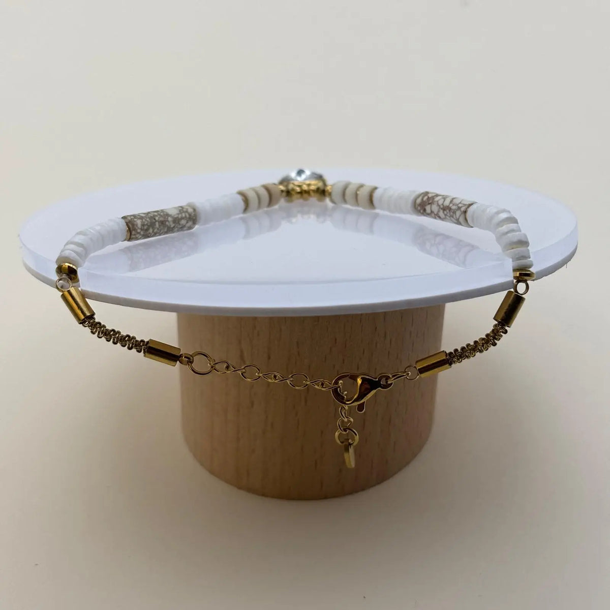 Bracelet doré avec des perles plates blanches marbrées et beiges avec un médaillon brillant