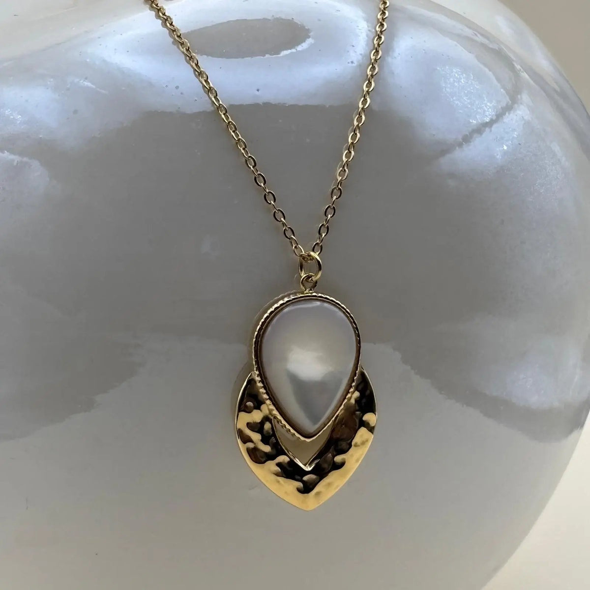 Un collier doré avec médaillon goutte dorée et perle nacrée en acier inoxydable