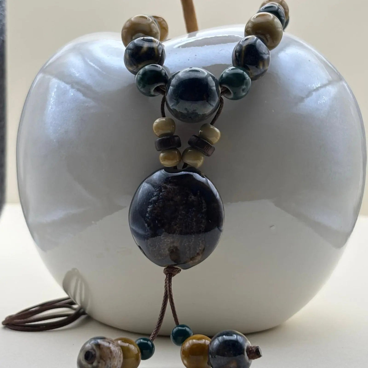 Un collier fantaisie ethnique avec lien en nylon marron réglable avec perles céramique et médaillon couleur bleu canard