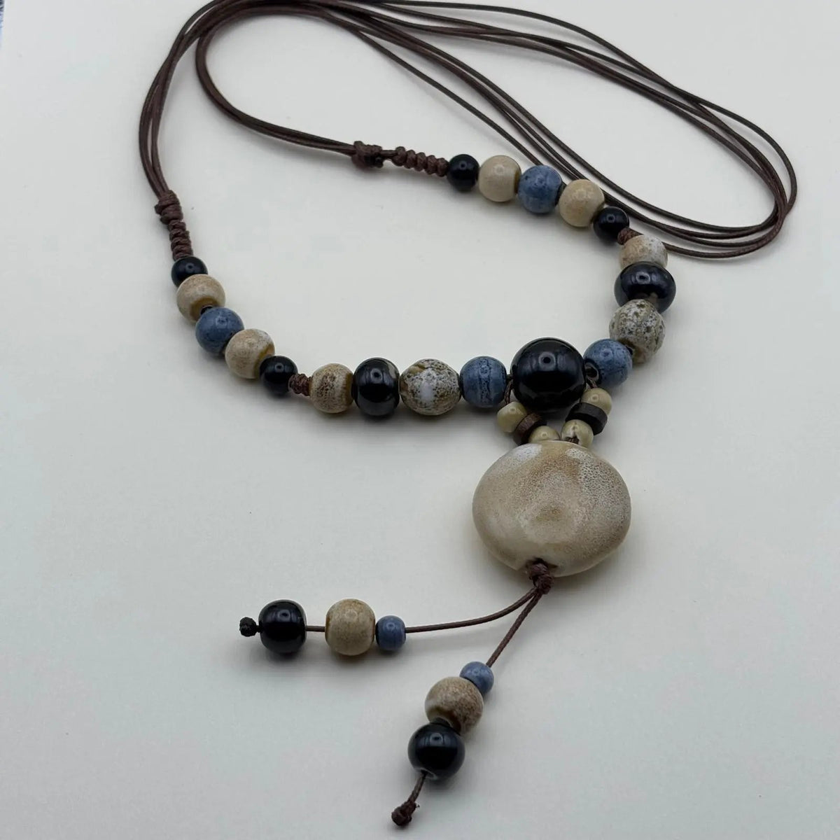 Collier fantaisie ethnique avec un lien en nylon marron réglable avec perles céramique et médaillon couleur écru