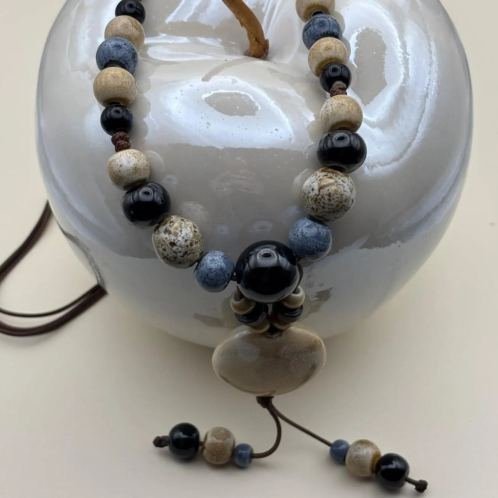Un collier fantaisie ethnique avec lien en nylon marron réglable avec perles céramique et médaillon couleur écru