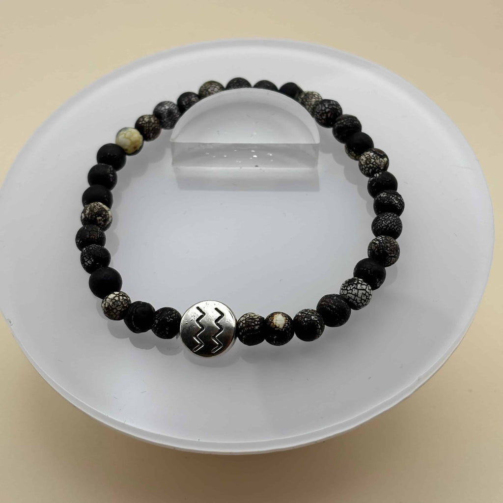 Un bracelet en perles sur élastique avec perles en porcelaine et en verre et médaillon avec le signe du verseau