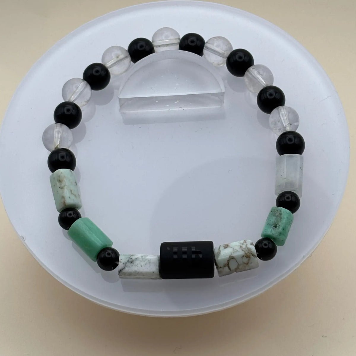 Bracelet formé de perles noires, blanches et vertes avec un cylindre noir gravé au centre