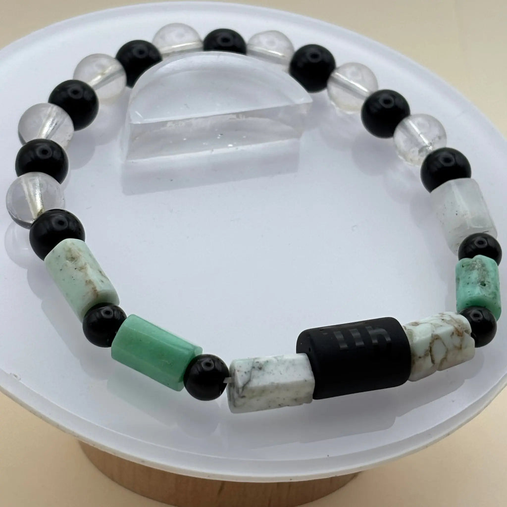 Bracelet mélangeant perles transparentes, noires et cylindriques vert clair autour d’un cylindre noir gravé