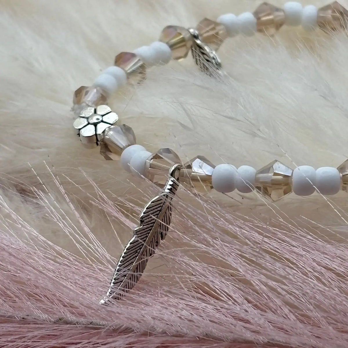 Vue de près d'un bracelet en perles artisanal avec breloques plumes et fleurs et perles en verre blanche sur élastique