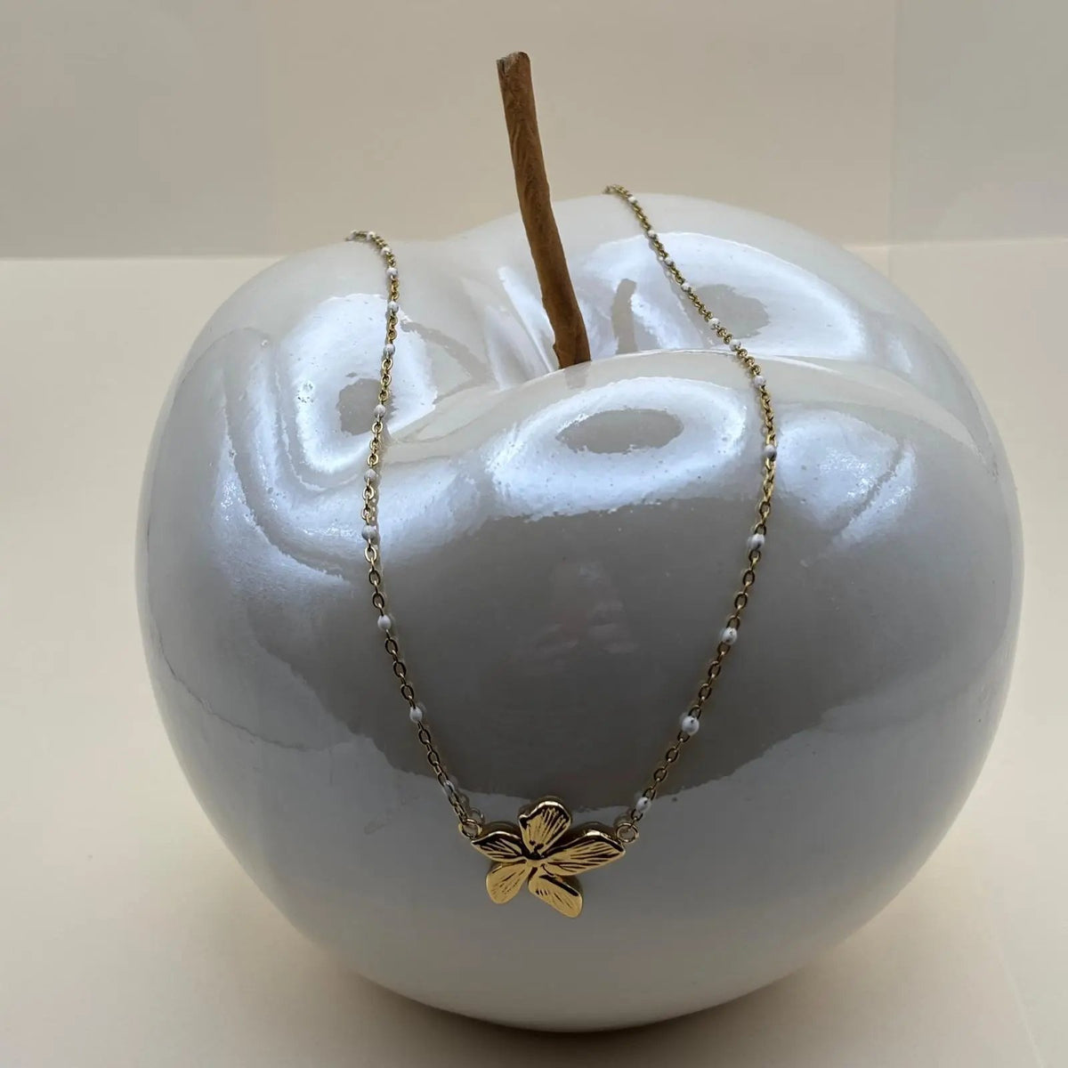 Un collier avec des petits maillons dorés et pendentif central avec une fleur dorée