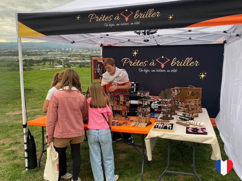 Un stand de vente de bijoux fantaisie sur un marché artisanal avec des clients devant Image