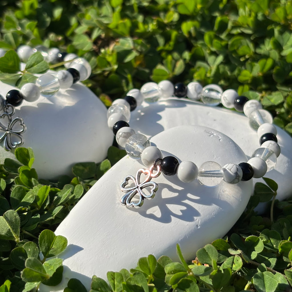 Un ensemble de deux bracelets artisanaux en perles d'howlite et obsidienne et une breloque en forme de trèfle argenté