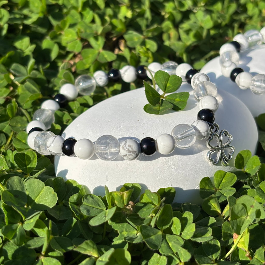 Vue de près d'un ensemble de deux bracelets artisanaux en perles d'howlite et obsidienne et une breloque en forme de trèfle argenté