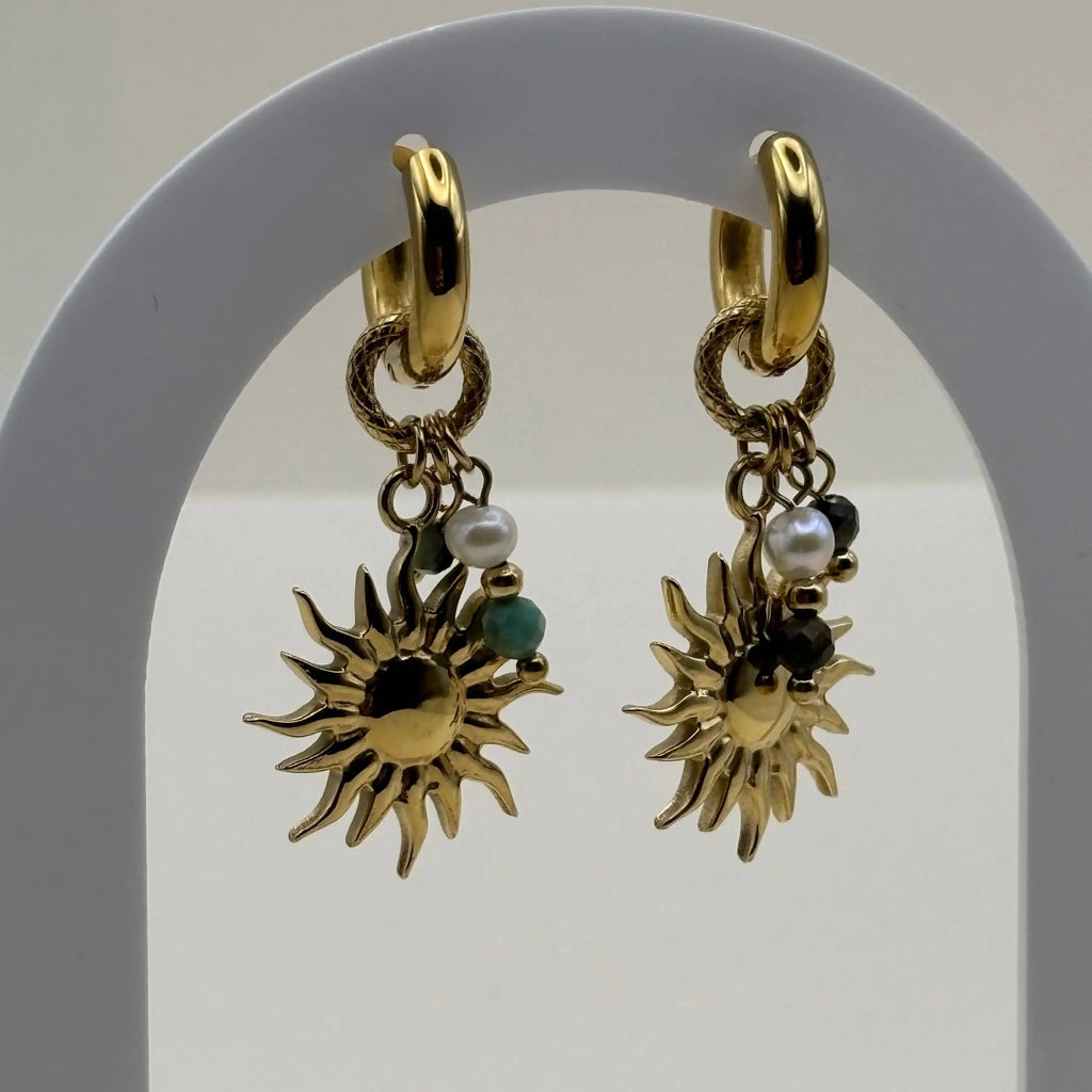 Vue de près de boucles d'oreilles dorées créoles pendentifs en forme de soleil  et perles colorées