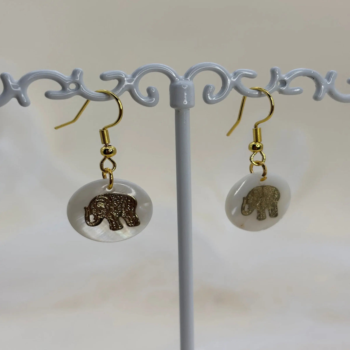 Une paire de boucles d'oreilles avec une pastille nacrée et dessin d'un éléphant