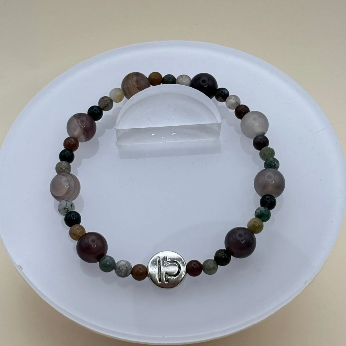 Bracelet de petites perles colorées aux tons naturels avec un médaillon argenté gravé en façade