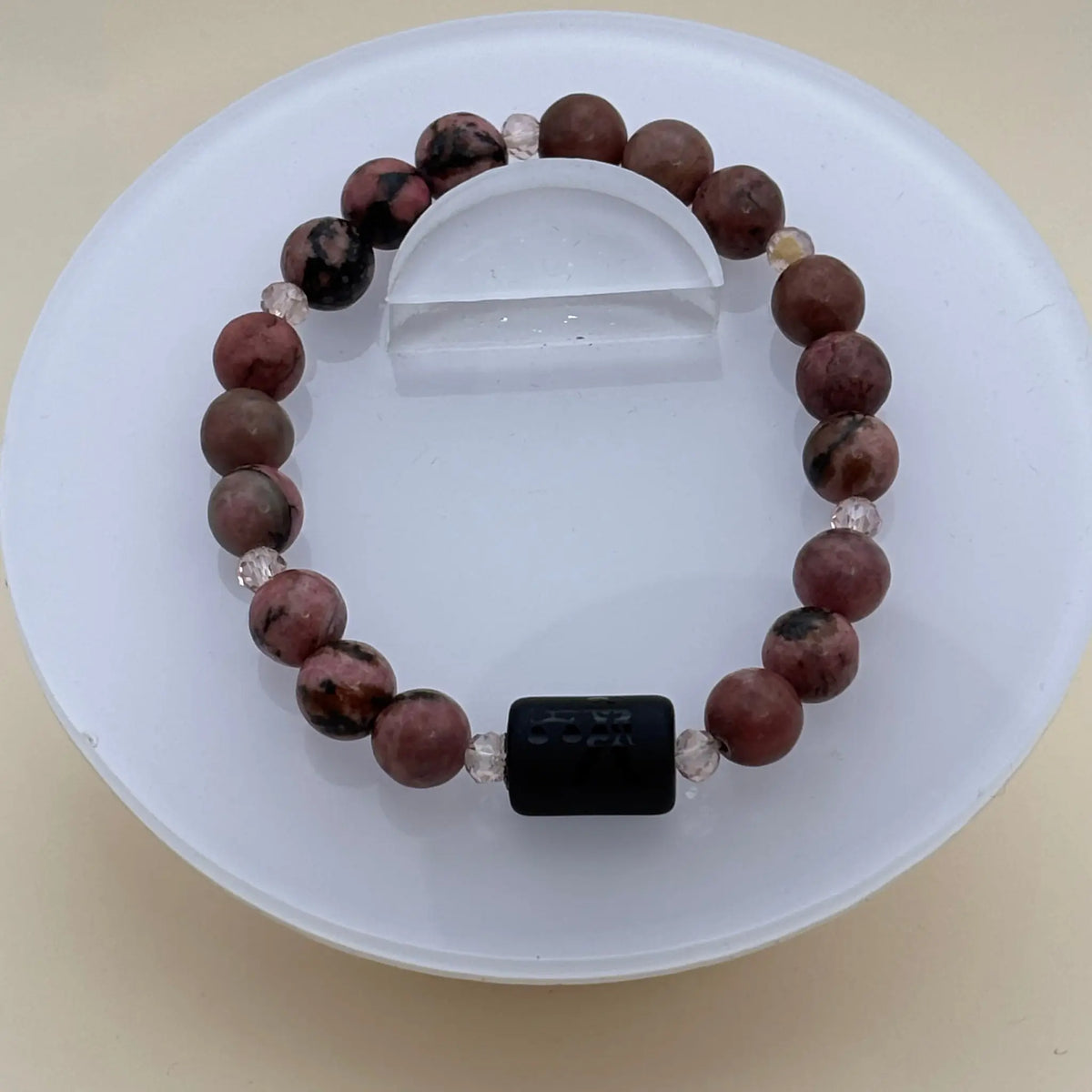 Bracelet de perles rosées et sombres alternées rehaussé d’un cylindre noir gravé au centre