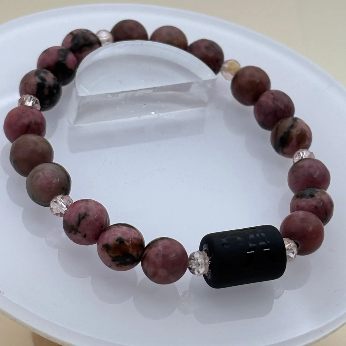 Bracelet composé de perles rondes rose foncé et noir avec un cylindre noir gravé en élément central