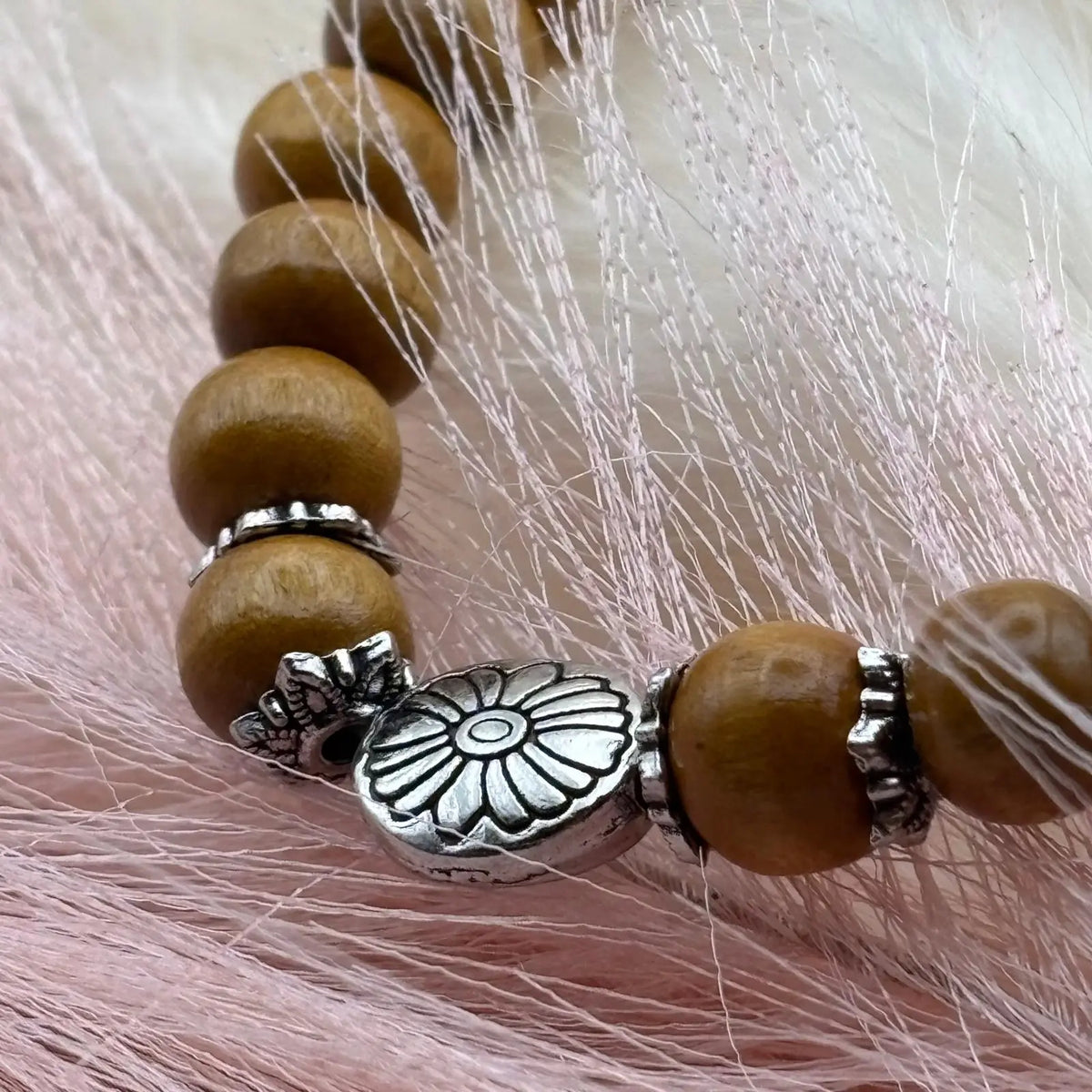 Vue de près d'un bracelet en perles artisanal avec une breloque en forme de fleur argentée et des perles en bois