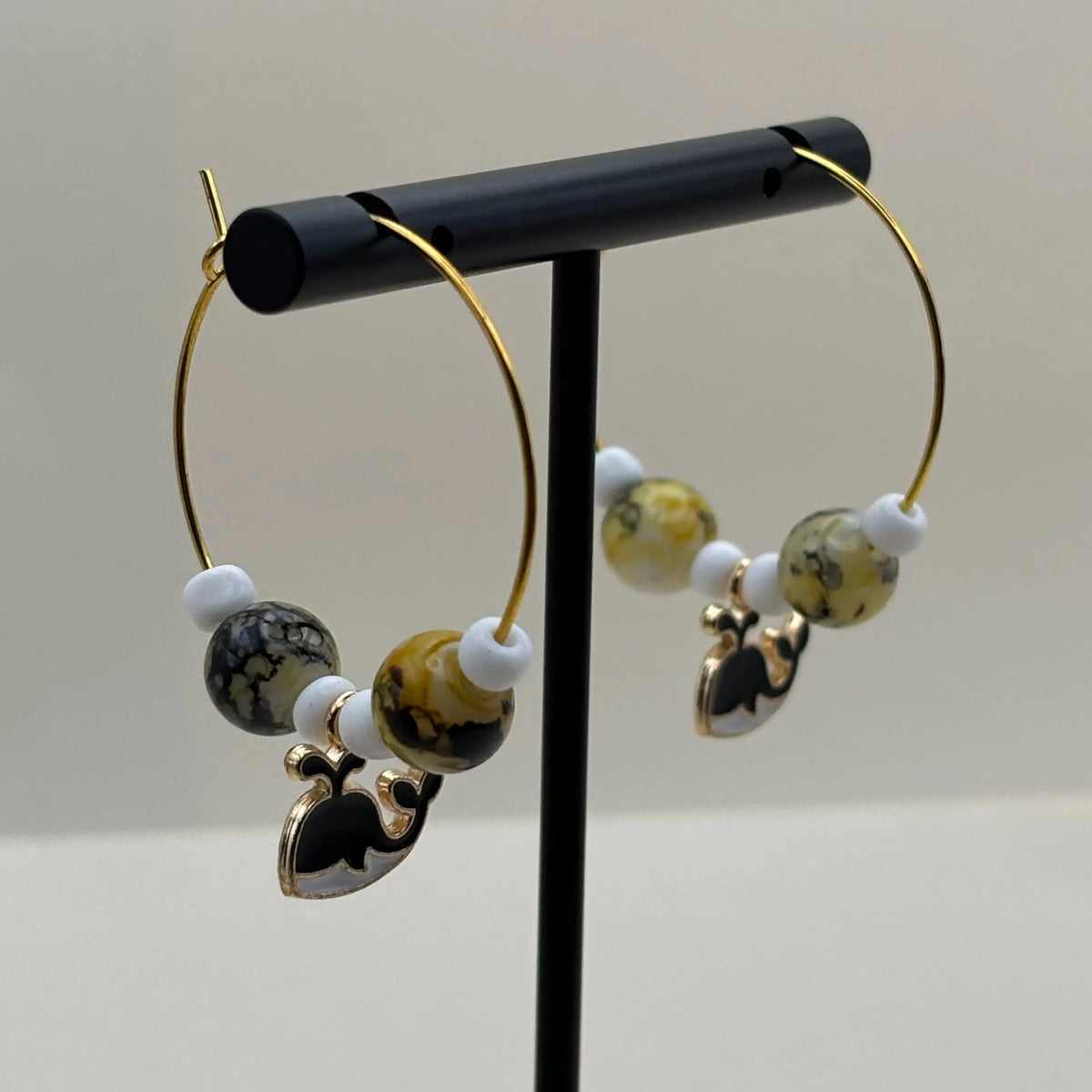 Des boucles d'oreilles créole dorées avec breloque baleine noire et blanche et perles en acrylique