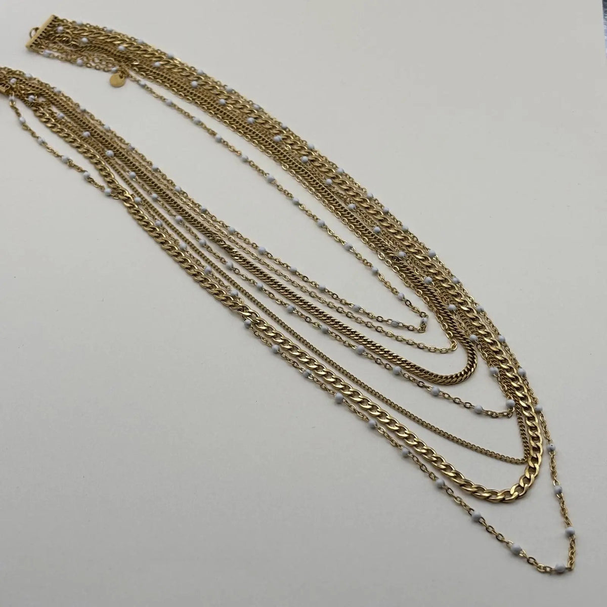 Vue de près d'un collier multirangs chaine à mailles différentes et boules céramiques blanches en acier inoxydable