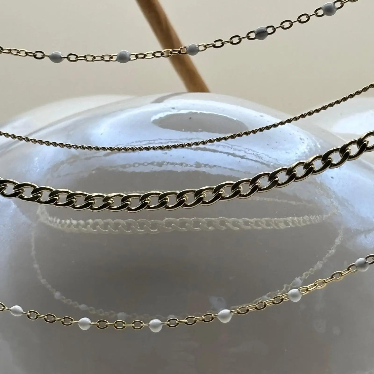 Un collier multirangs chaine à mailles différentes et boules céramiques blanches en acier inoxydable
