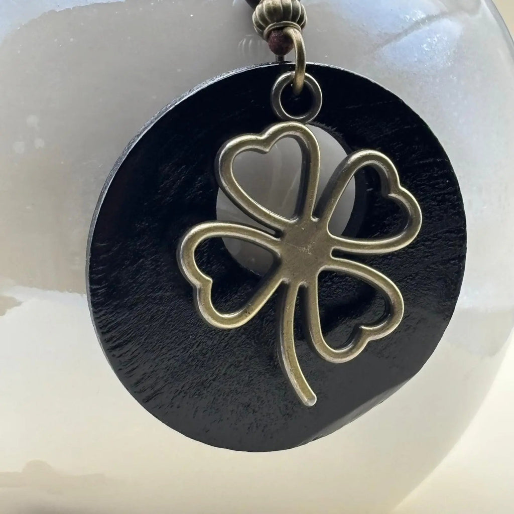 Un collier fantaisie en médaillon en bois noir motif porte bonheur trèfle et cordon en cuir