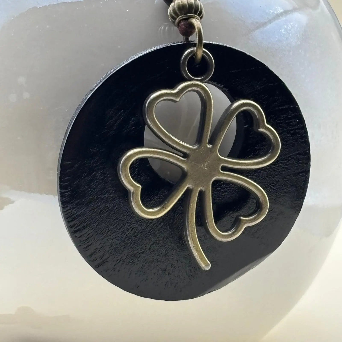 Un collier fantaisie en médaillon en bois noir motif porte bonheur trèfle et cordon en cuir