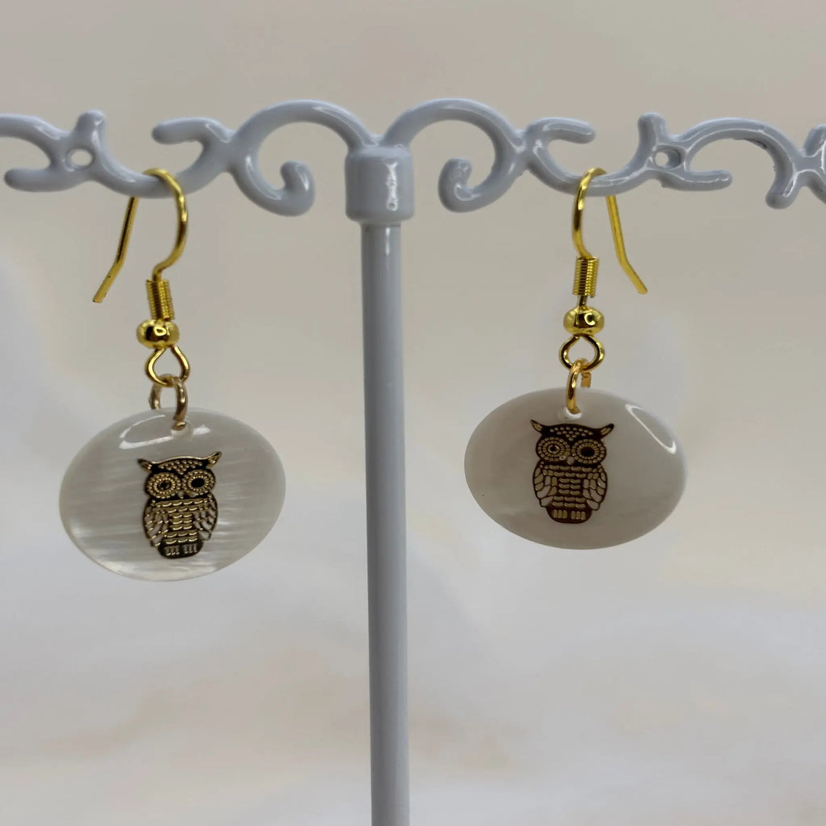 Une paire de boucles d'oreilles avec une pastille nacrée et dessin d'un hibou