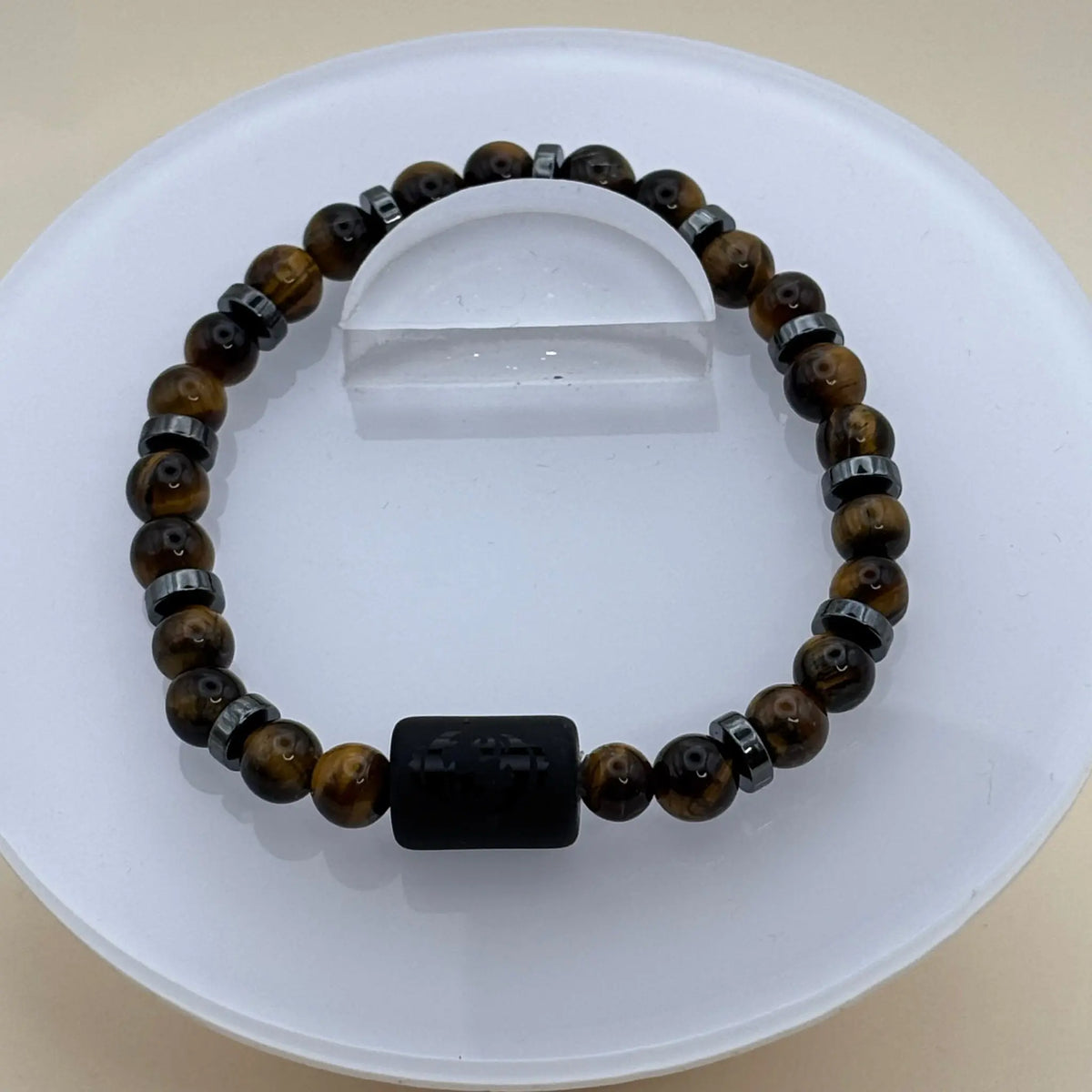 Bracelet aux perles marron doré et anneaux métalliques gris avec un cylindre noir gravé au centre