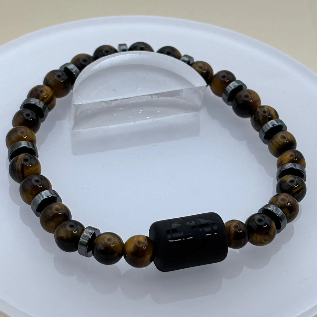 Bracelet formé de perles brun doré et anneaux métalliques gris autour d’un cylindre noir gravé