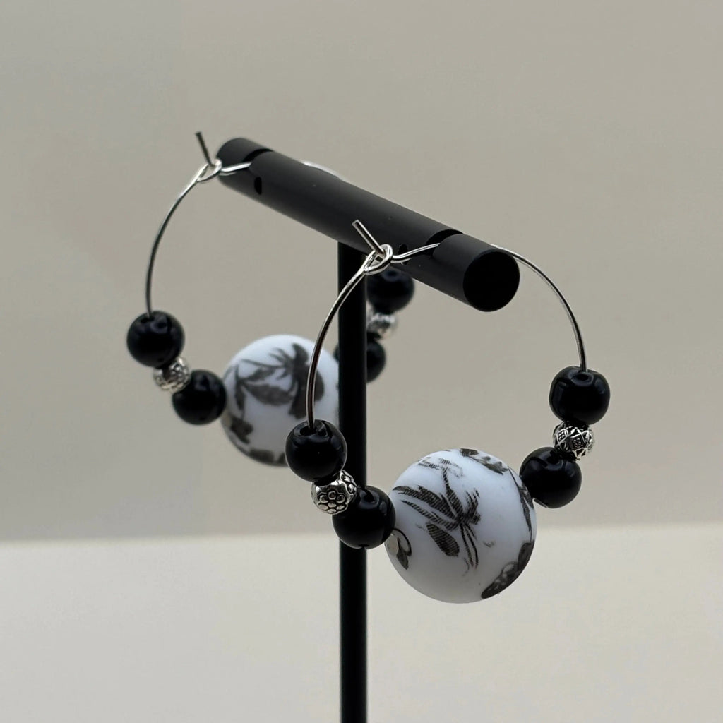 Une paire de boucles d'oreilles artisanales créole avec une perle fleurie et deux perles noires