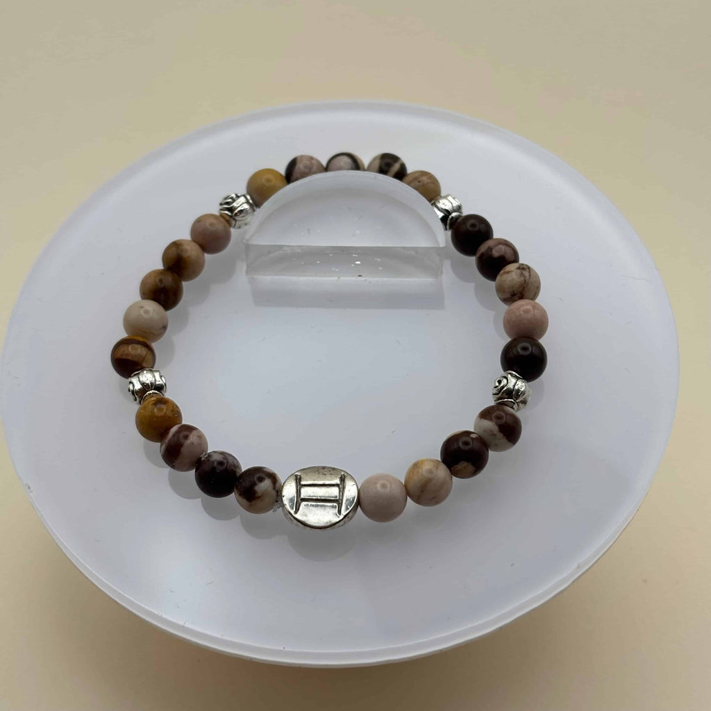 Un bracelet en perles sur élastique avec perles en porcelaine et en verre et médaillon avec le signe du gémeaux