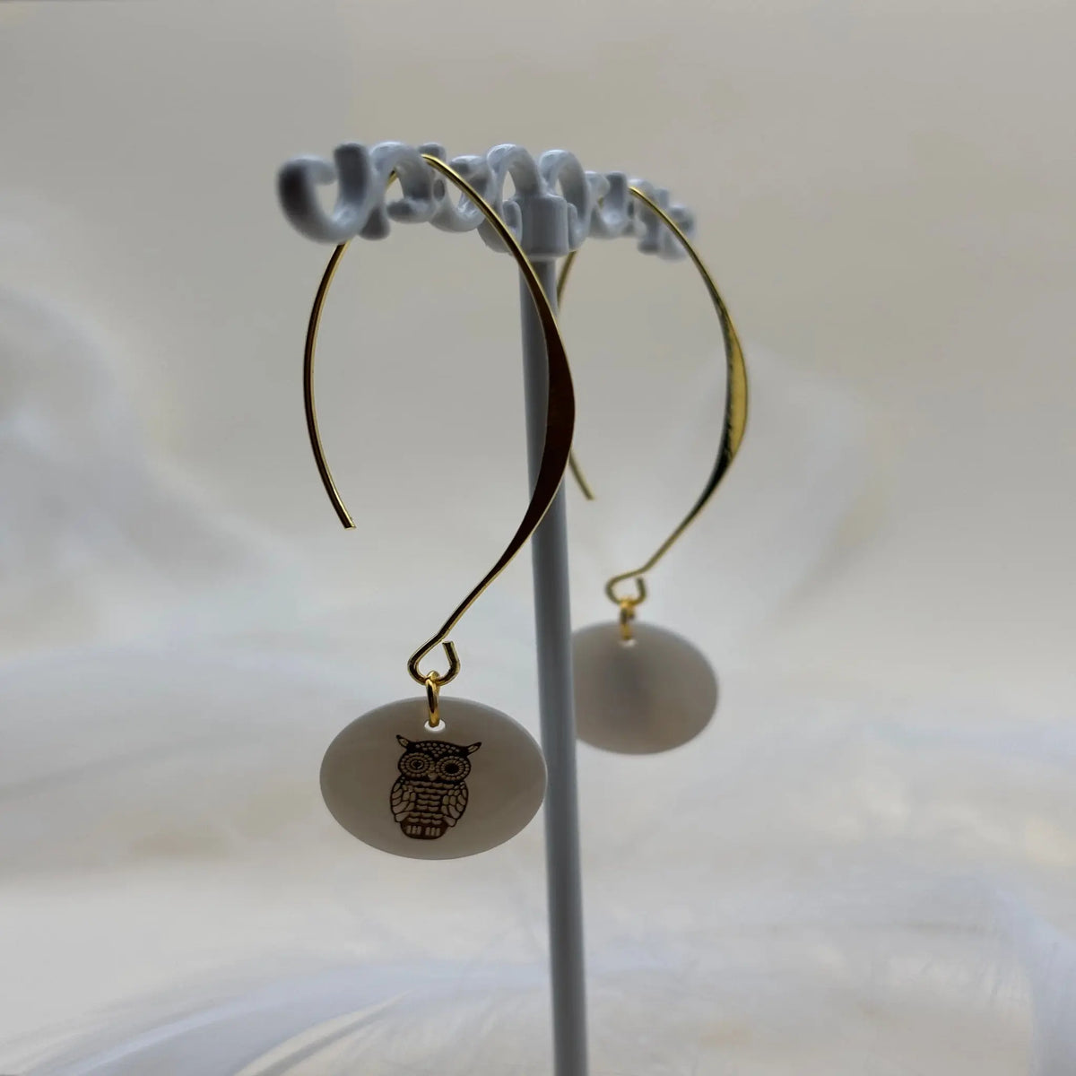 Une paire de boucles d'oreilles pendentif avec une pastille nacrée et dessin de hibou doré