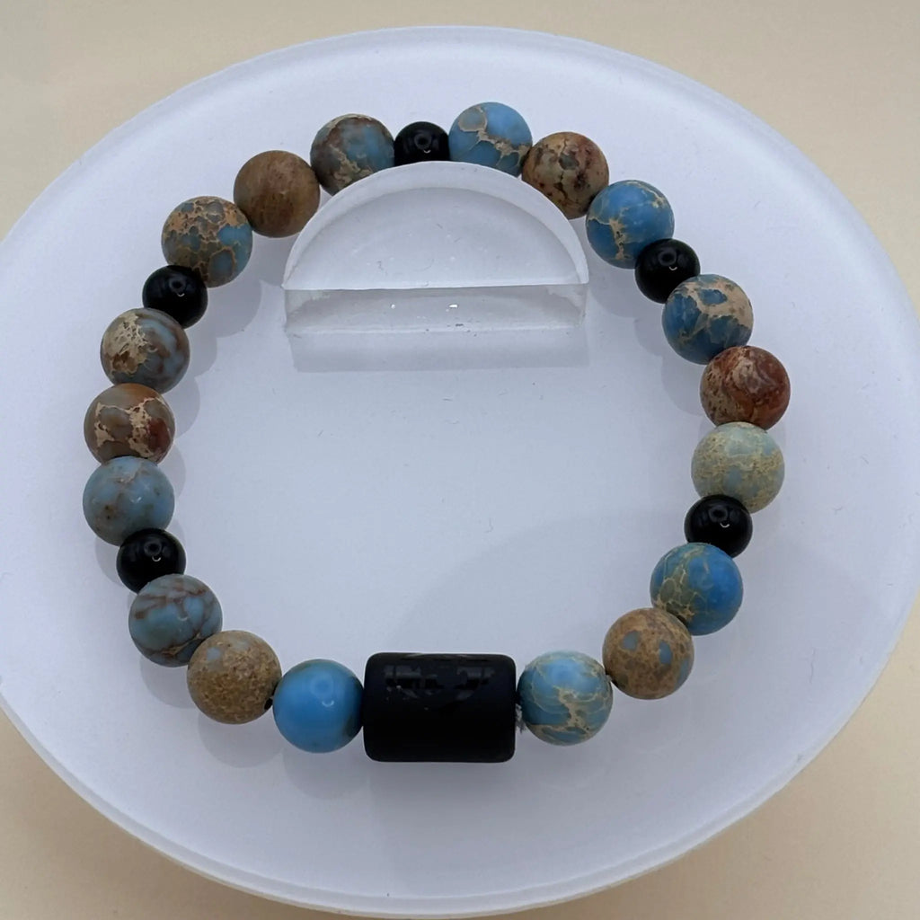 Bracelet composé de perles aux tons bleus et bruns avec un cylindre noir gravé comme élément central