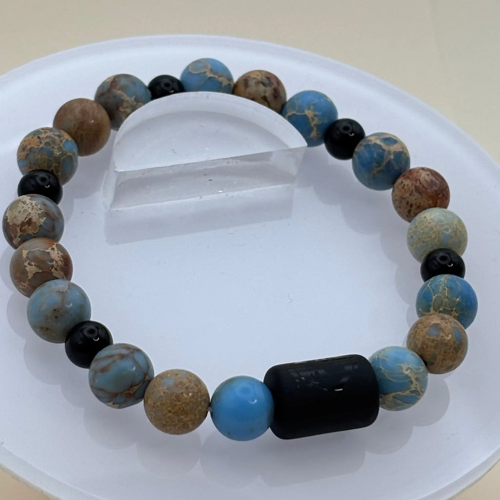 Bracelet composé de perles aux nuances bleues et brunes avec une pièce centrale cylindrique noire gravée