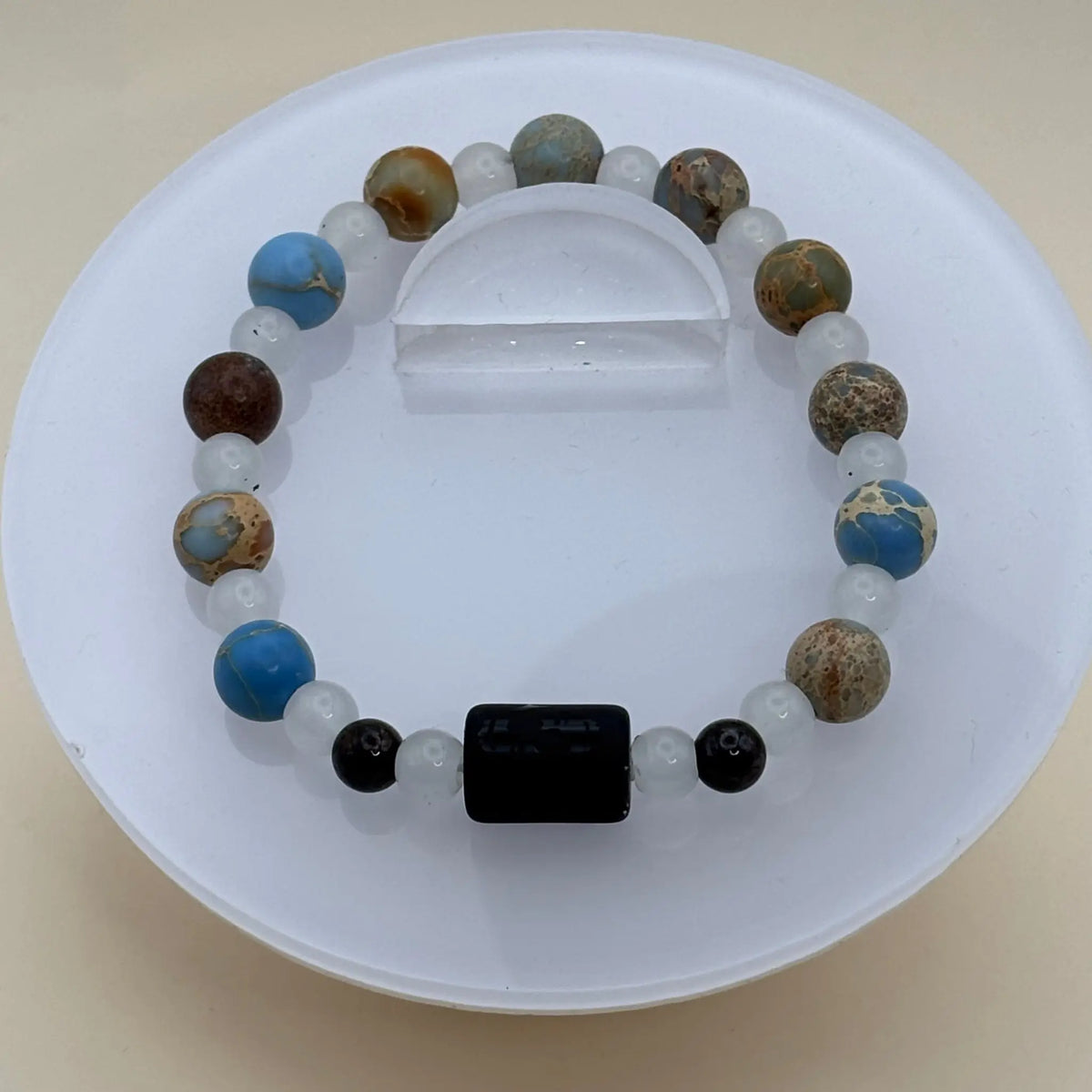 Bracelet alternant perles blanches et perles bleues marbrées avec un cylindre noir gravé en élément central
