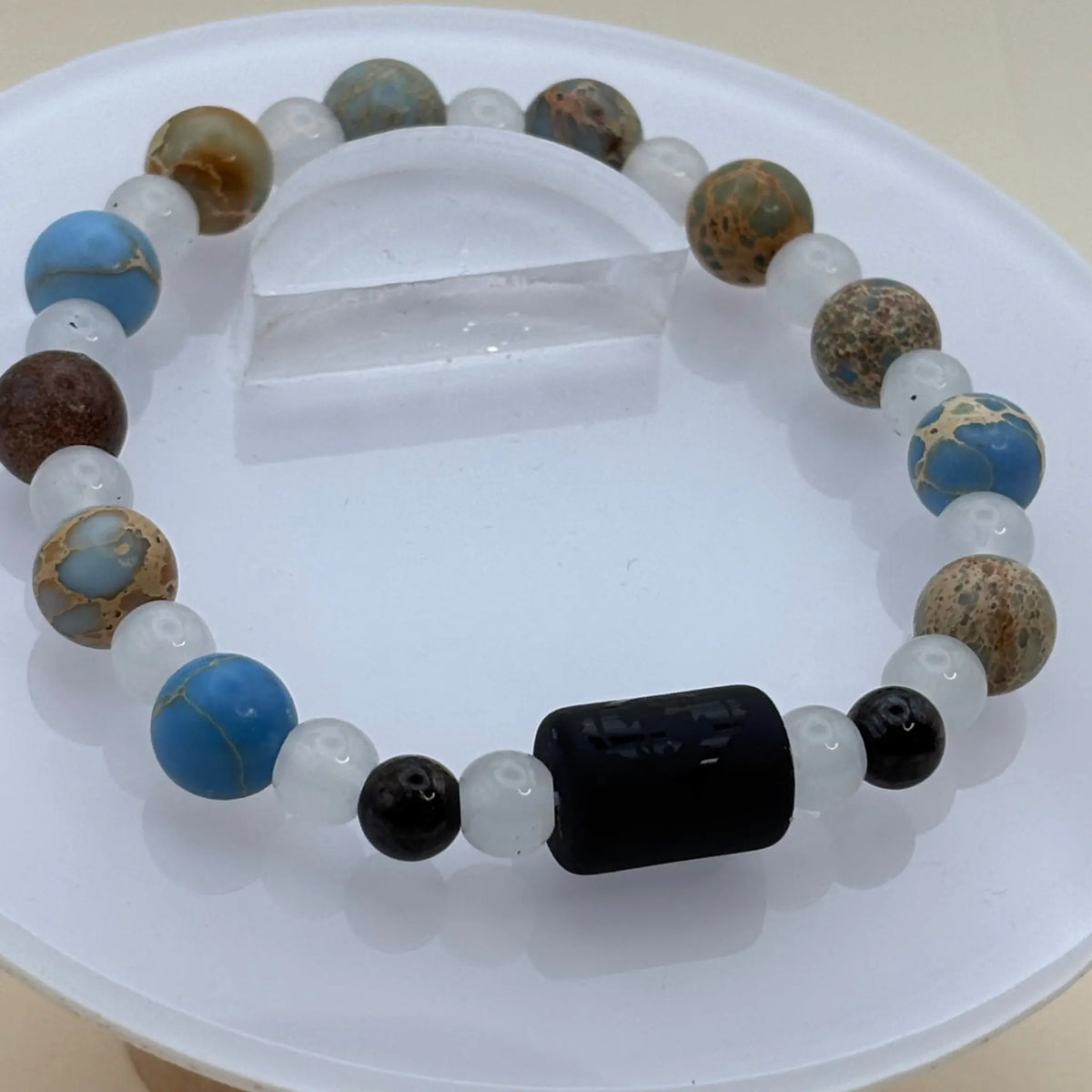 Bracelet composé de perles blanches, bleues et brunes agrémenté d’un cylindre noir gravé placé en avant