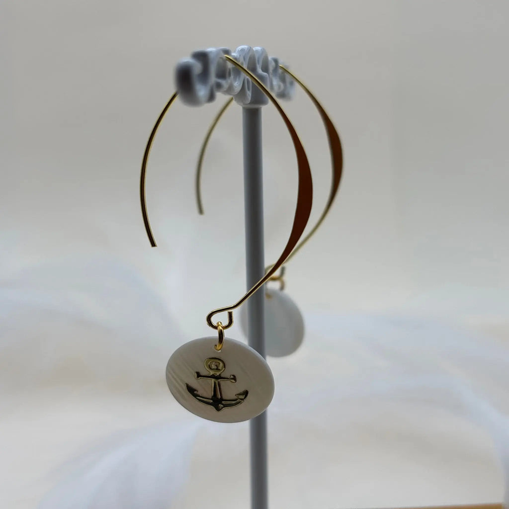 Une paire de boucles d'oreilles pendentif avec une pastille nacrée et dessin d'une ancre de marine