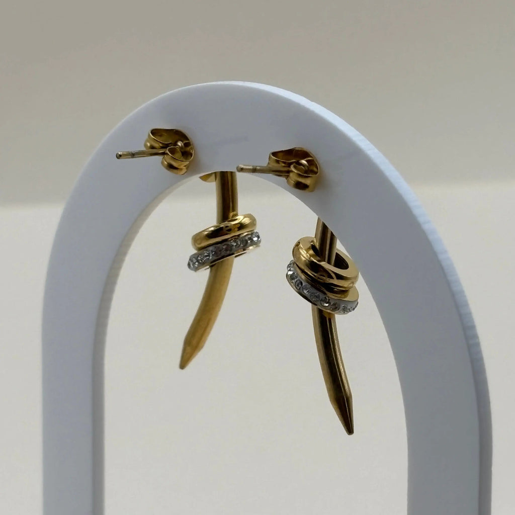 Une paire de boucles d'oreilles dorées avec motif clou et strass en acier inoxydable 