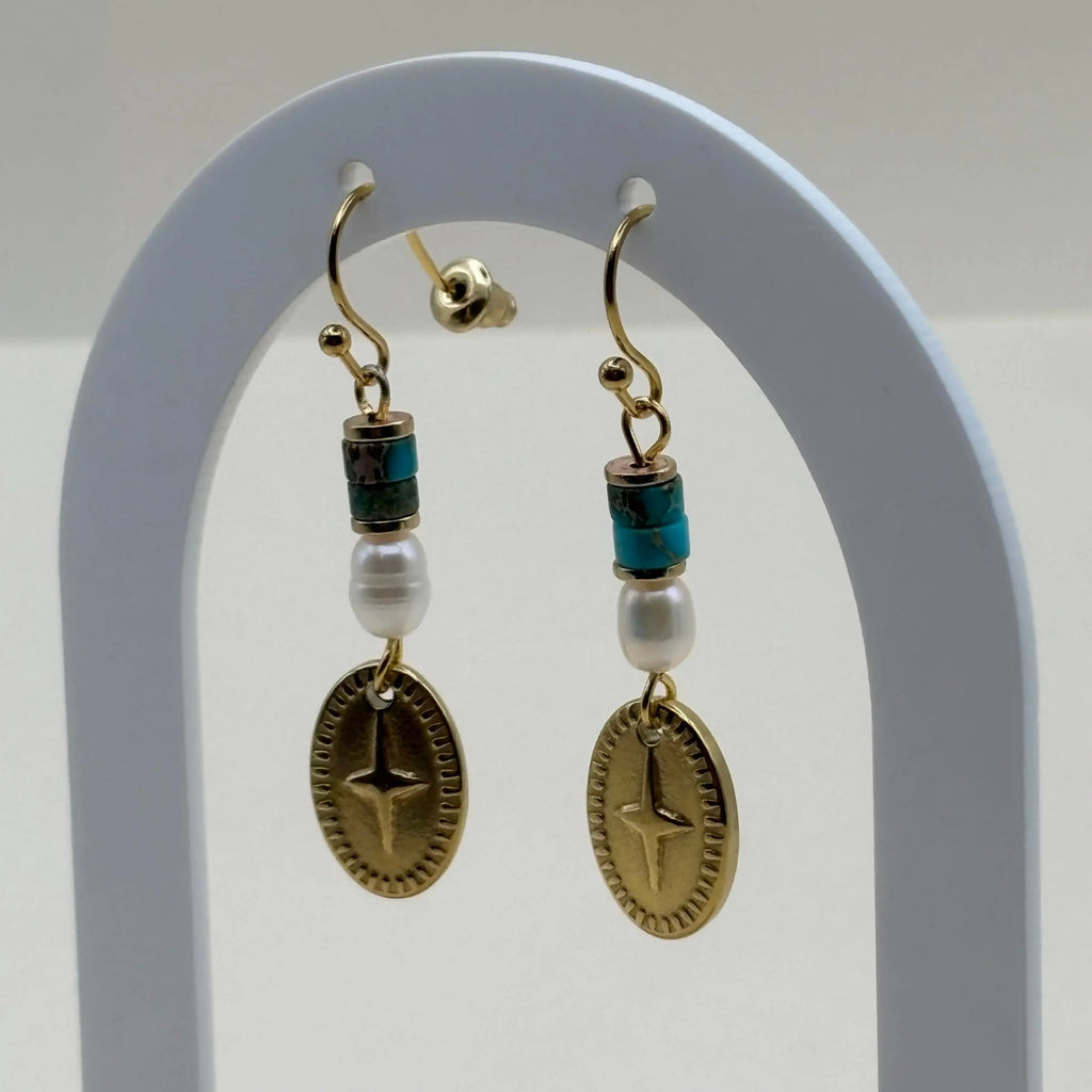 Des boucles d'oreilles attache dorée avec breloque ovale rose des vents et perles bleues et blanches