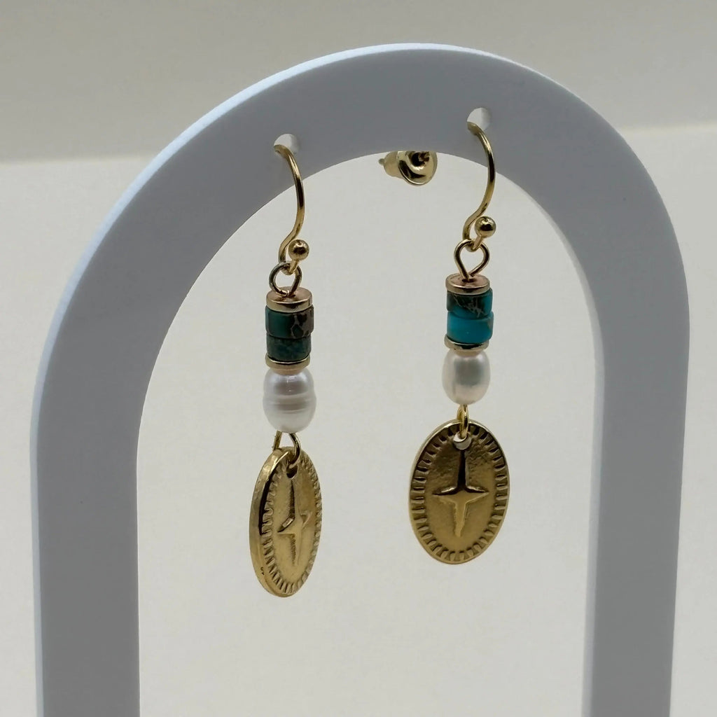 Une paire de boucles d'oreilles attache dorée avec breloque ovale rose des vents et perles bleues et blanches