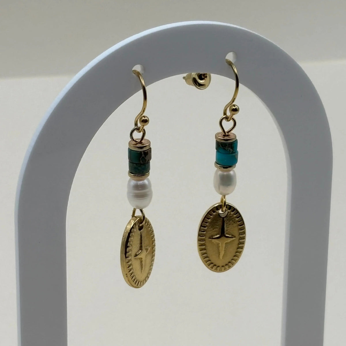 Une paire de boucles d'oreilles attache dorée avec breloque ovale rose des vents et perles bleues et blanches